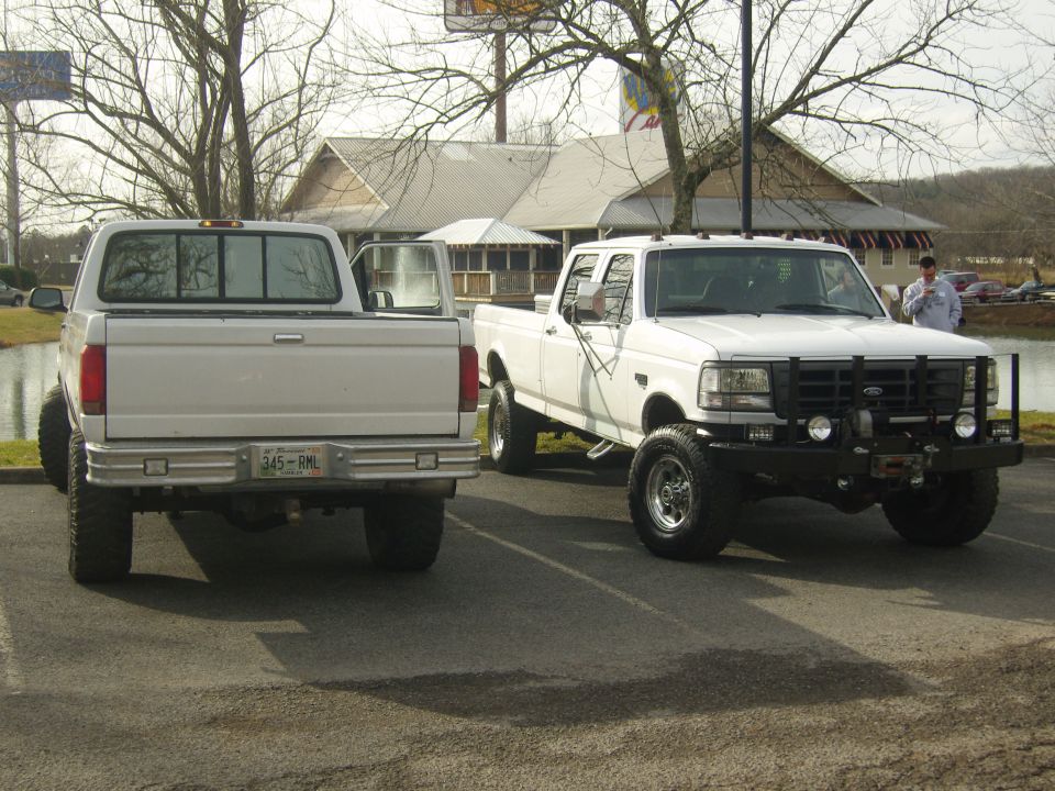 Two white Ford pickup trucks parked side-by-side. The truck on the right has a black grille guard and winch