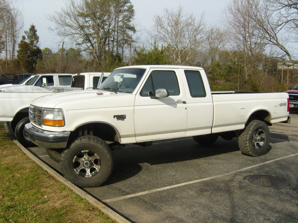 White four-door pickup truck with lifted suspension and aftermarket wheels, parked outdoors