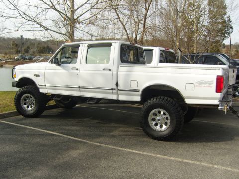 2007 Ford Mustang - A white lifted crew cab pickup truck is parked in a lot, with another vehicle visible behind it. The truck has "4x4 OFF ROAD" decals on the…