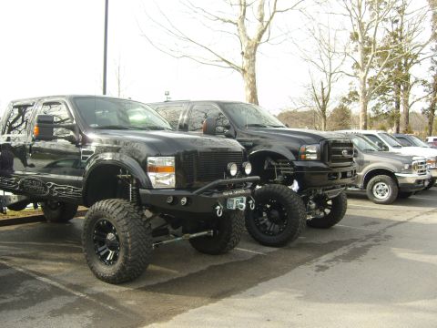 2007 Ford Mustang - Several lifted pickup trucks are parked in a lot on a cloudy day.
