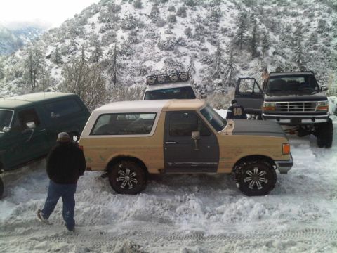 1986 Ford Bronco - Several off-road vehicles are parked in a snowy landscape, with one Bronco showing mismatched door colors.