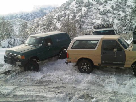 1986 Ford Bronco - Two Ford Bronco SUVs navigate a snowy mountain road.
