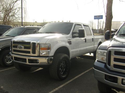 2007 Ford Mustang - A white Ford F-Series truck is parked next to another truck, with a sign visible in the background.