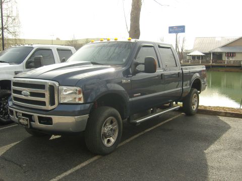 2007 Ford Mustang - A dark blue crew cab pickup truck is parked in a lot next to another truck, with a body of water and buildings in the background.