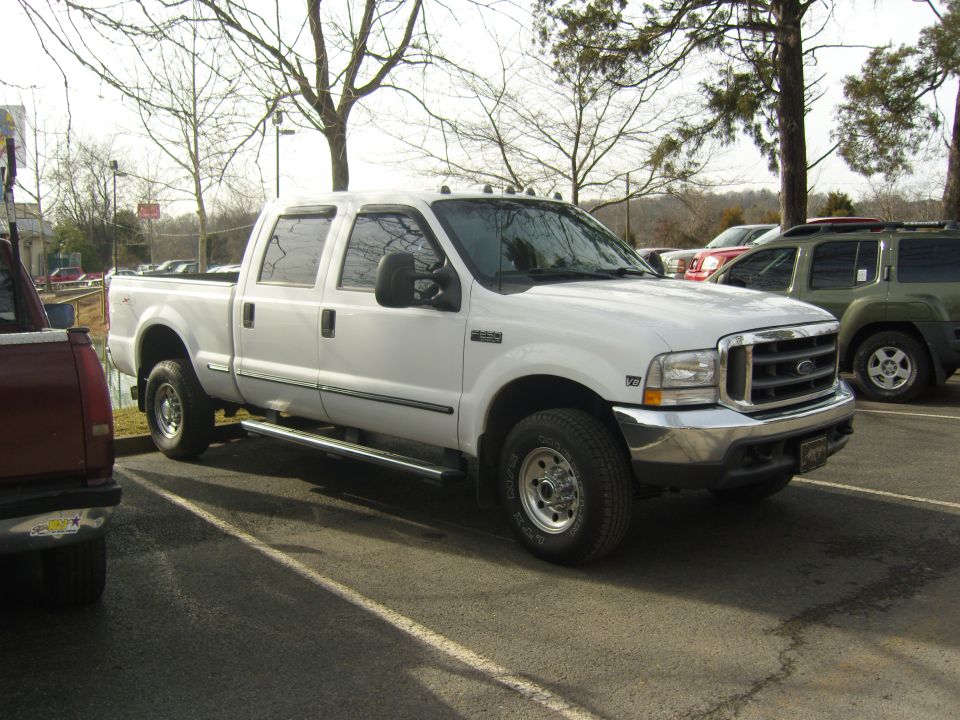 White Ford F-250 Super Duty pickup truck parked in a lot, with a red truck and green SUV nearby