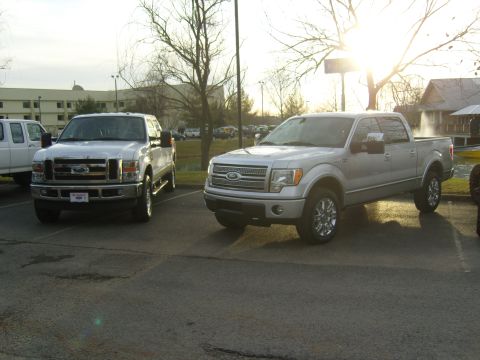 2007 Ford Mustang - Two Ford pickup trucks are parked in a lot with a building and trees in the background.