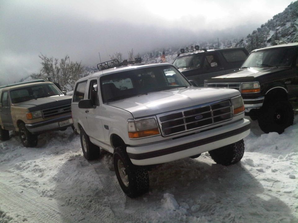 White Ford Bronco in snow, front 3/4 view. Other Broncos visible