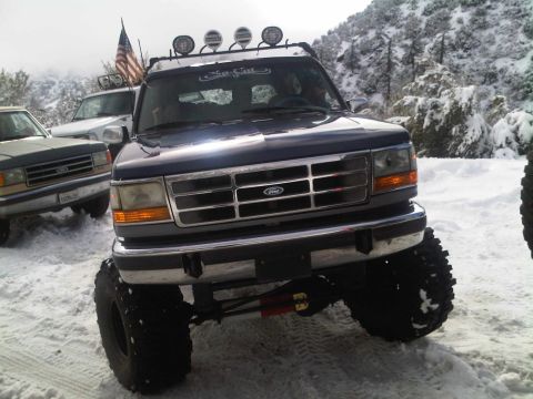 1986 Ford Bronco - Modified Ford Bronco with off-road tires and lights sits in a snowy landscape.