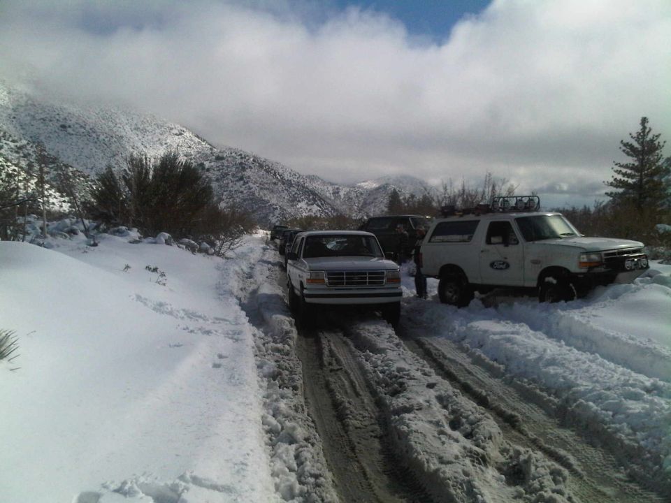 White Ford Bronco with roof rack and off-road lights on a snow-covered road