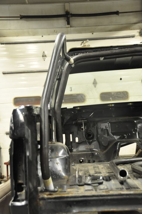 1996 Ford Bronco - A roll cage is being fitted into the interior of a vehicle, showing the bare metal floor and rear structure.