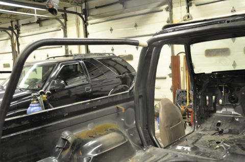 1996 Ford Bronco - A black SUV is visible in the background of a garage, partially obscured by the interior of another vehicle undergoing modifications.