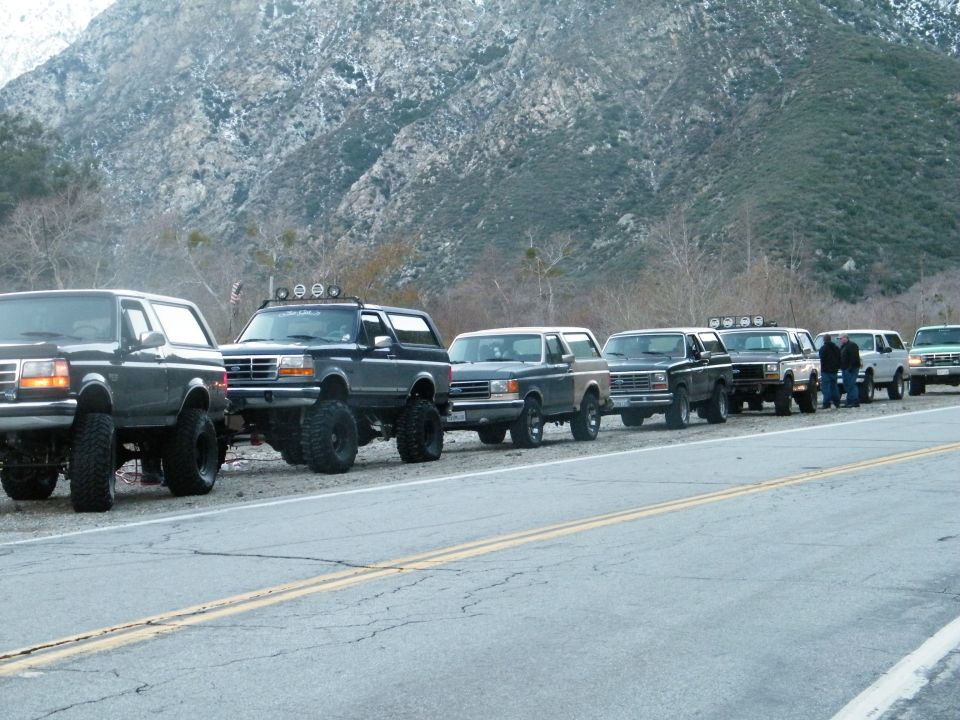 Several lifted Ford Broncos lined up on a road with mountains in the background