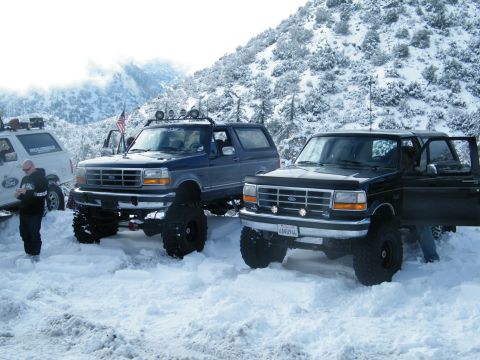 1982 Ford Bronco - Two lifted Ford Broncos sit in a snowy mountain landscape.
