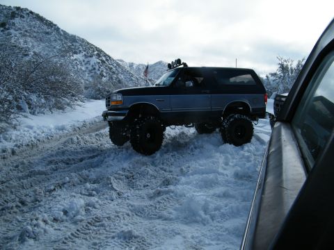 1982 Ford Bronco - A lifted Ford Bronco navigates a snow-covered trail with a mountain backdrop.