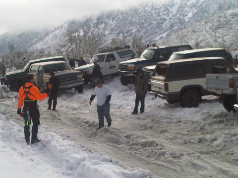 1986 Ford Bronco - Multiple SUVs and trucks are gathered in a snowy, mountainous area, with several people standing around them.