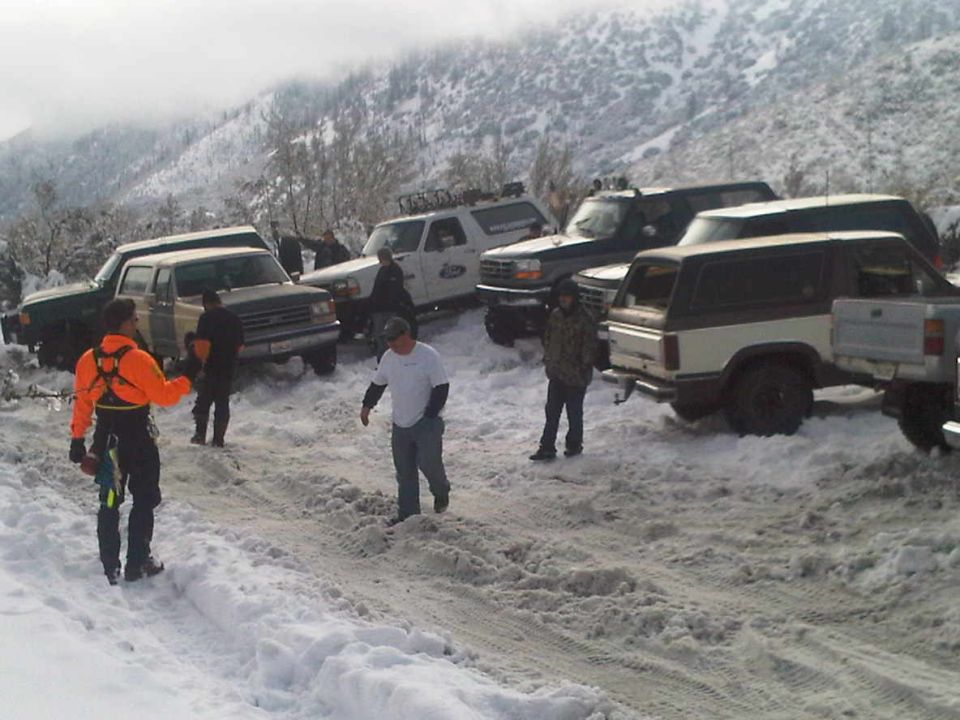 Several SUVs and trucks parked in snow, some with people around them. A white and brown SUV is in the foreground