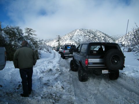 1982 Ford Bronco - Multiple SUVs, including a Ford Bronco, navigate a snow-covered mountain road.