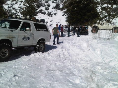 1986 Ford Bronco - A group of people stand around several vehicles stuck in the snow, including a modified white Ford Bronco.