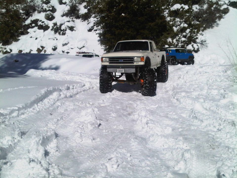 White 1987 Ford F-150 pickup truck with large off-road tires in snow