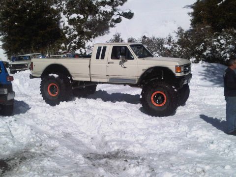 1986 Ford Bronco - A heavily modified pickup truck sits in a snowy landscape, with another vehicle partially visible to its left.