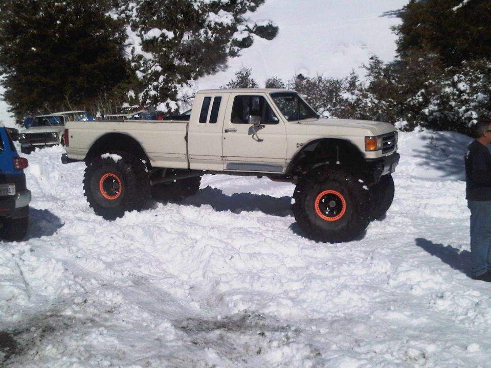 lifted white pickup truck with big tires in the snow, another vehicle to the left