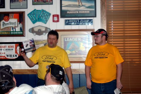 2007 Ford Mustang - Two men wearing Ford-themed shirts stand indoors, with various framed items and memorabilia on the wall behind them.