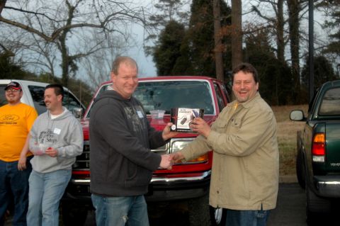 2007 Ford Mustang - Two men exchange a gift box in front of a red pickup truck, with another vehicle parked nearby.
