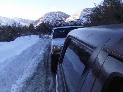 1986 Ford Bronco - Two SUVs navigate a snowy mountain pass, one equipped with a roof-mounted light bar.
