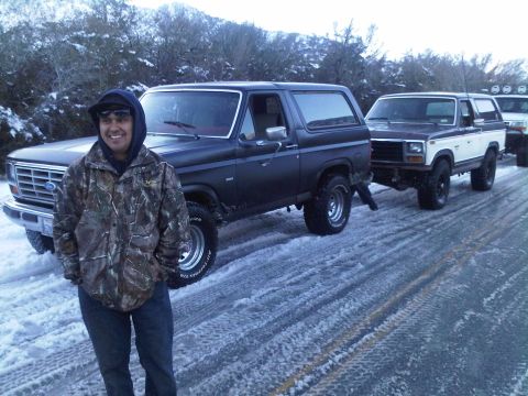 1986 Ford Bronco - Three Ford Broncos parked on a snowy road with a man in the foreground.