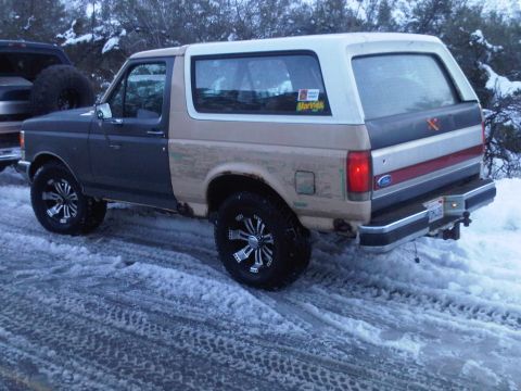 1986 Ford Bronco - Ford Bronco with aftermarket wheels in snowy conditions. Another vehicle is partially visible.