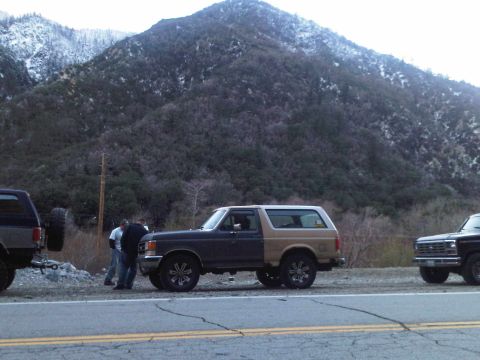 1986 Ford Bronco - Two Ford vehicles parked on the side of a road with a mountain range in the background.