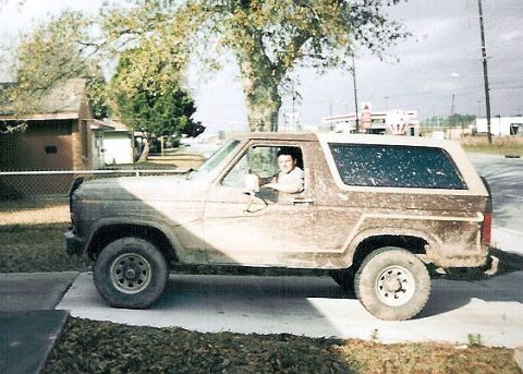1983 Ford Bronco - A mud-covered 1980s Ford Bronco is parked on a concrete driveway, with a person visible in the driver's seat.