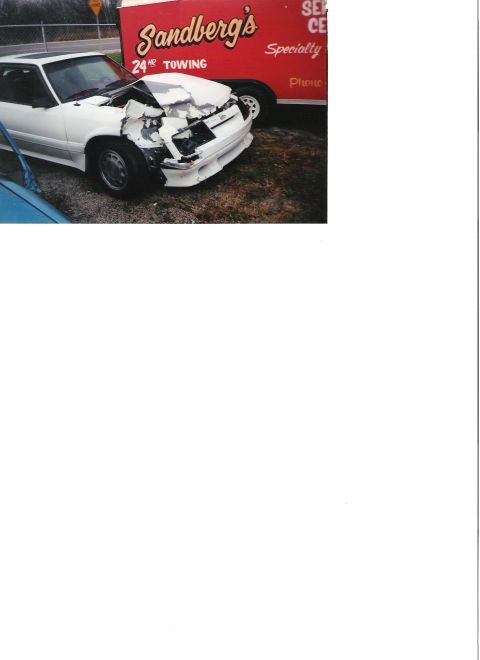 1986 Ford Mustang - Damaged white coupe, likely a 1987 model, sits beside a Sandberg's towing trailer.