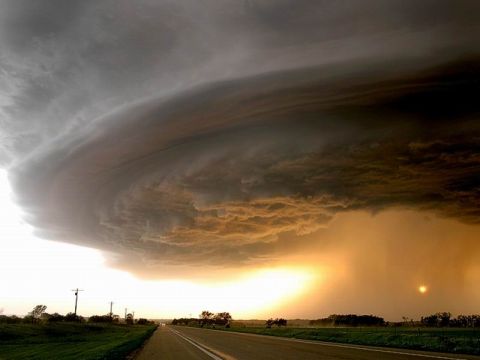 1991 Ford Bronco - A massive supercell thunderstorm looms over a desolate rural highway as the sun sets, casting an eerie orange glow.