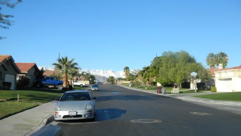 1997 Ford Ranger - A residential street scene with a silver coupe in the foreground and a blue pickup truck parked in a driveway.