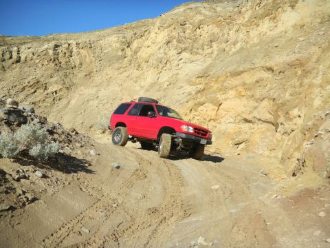 1997 Ford Ranger - Red SUV navigates a challenging off-road trail with steep, rocky terrain.