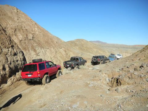 1997 Ford Ranger - A convoy of off-road vehicles navigates a challenging desert trail under a clear blue sky.