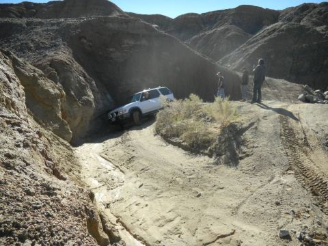 1997 Ford Ranger - A white SUV navigates a challenging off-road trail in a desert canyon landscape.