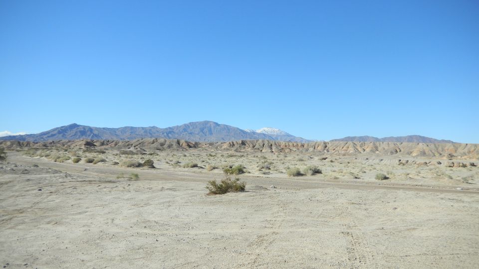 Desert wash with tire tracks below eroded badlands and snowy mountains