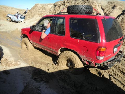 1997 Ford Ranger - Red Ford Explorer stuck in mud during off-road adventure, with another SUV visible in the background.