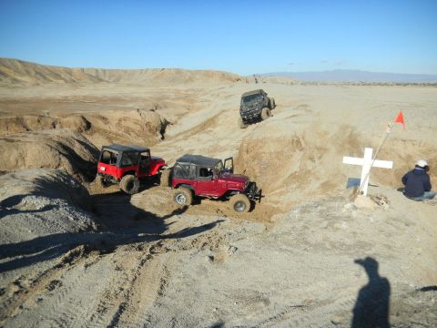 1997 Ford Ranger - Multiple Jeep Wranglers traverse a desert terrain, passing a memorial cross under a clear blue sky.