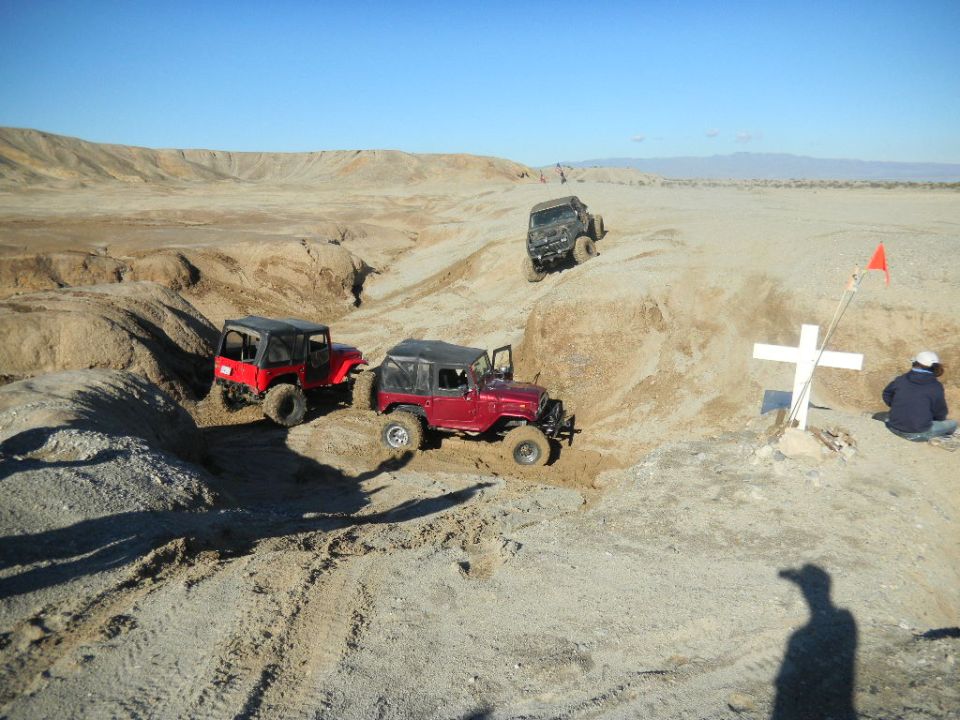 Red Jeep Wrangler off-roading in a desert with two other vehicles and a cross