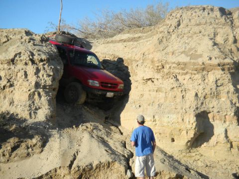 1997 Ford Ranger - A red SUV is stuck in a steep dirt embankment, with a person observing the situation.