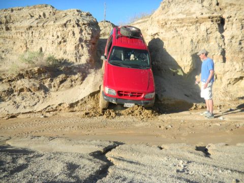 1997 Ford Ranger - A red 1997 Ford Explorer is stuck in a muddy ditch, with a man standing nearby observing the situation.