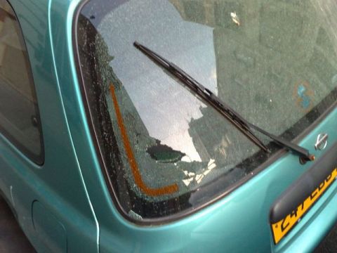 1991 Ford Crown Victoria - Close-up of a teal hatchback's rear window, showing cracked glass and a rear wiper. Yellow text is visible on the bumper.