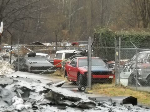 1982 Ford Bronco - Several vehicles are parked in a junkyard under a cloudy sky.