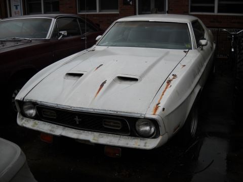 1982 Ford Bronco - A white 1971 Ford Mustang sits parked next to another vehicle, showing signs of wear and rust.