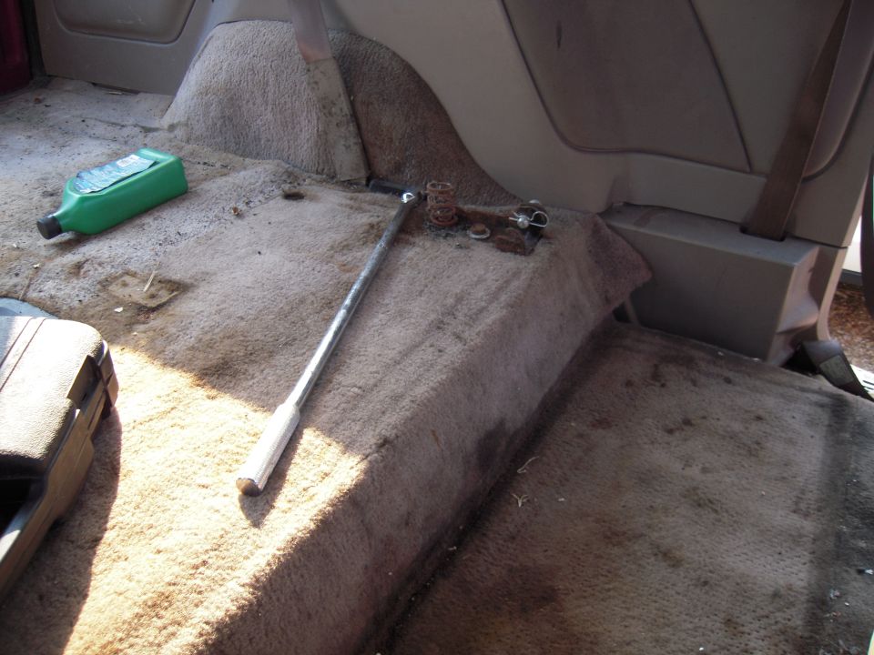 Breaker bar, rusty spring and hardware on dirty carpet inside a vehicle floor