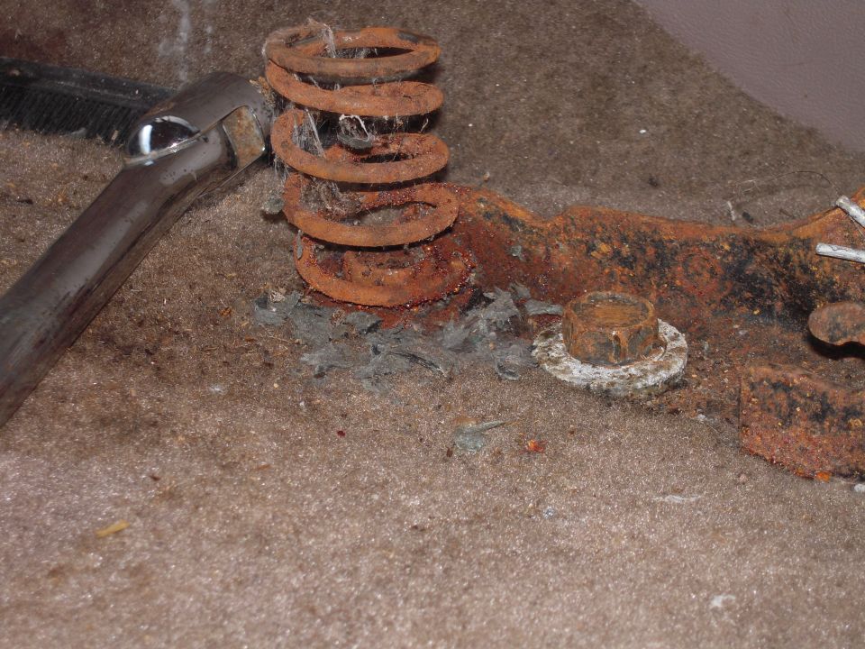 Rusty coil spring and corroded bracket sitting on dusty tan carpet