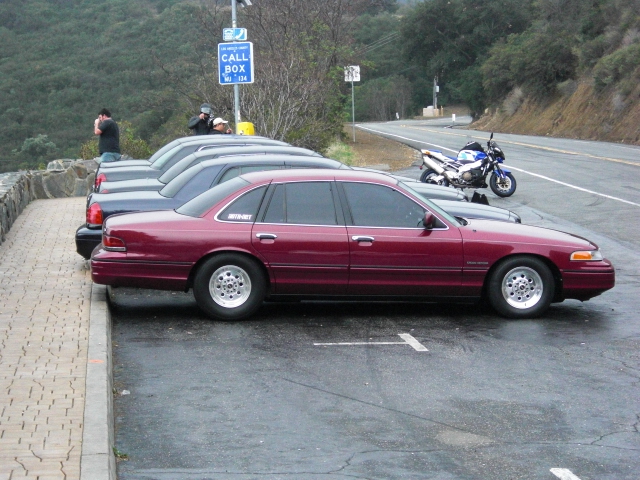 Maroon 1992 Ford Crown Victoria sedan with aftermarket wheels parked on a wet asphalt lot